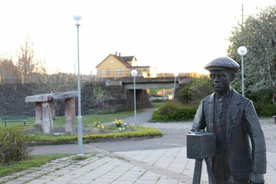 På Frinnaryds lilla torg finns en staty av bygdefotografen Oskar Jarén (1877-1954) som fotograferade i samhället redan på 1910-talet. I bakgrunden syns järnvägen och företaget Tvättcenter, som är ett av ett fåtal företag med anställda som finns kvar. Foto: David Spånberger