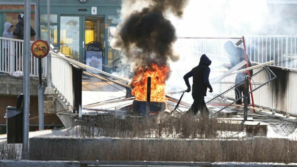 Personer gör en barrikad med brinnande bildäck och andra föremål vid Ringdansen centrum, i samband med upploppet i Navestad i Norrköping under påskdagen 2022.