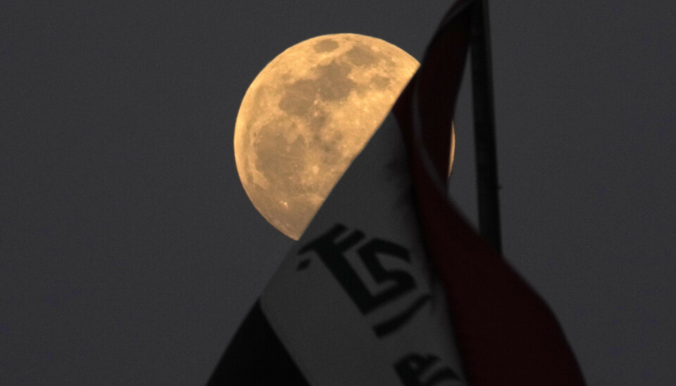 Månen lyser bakom en irakisk flagga.