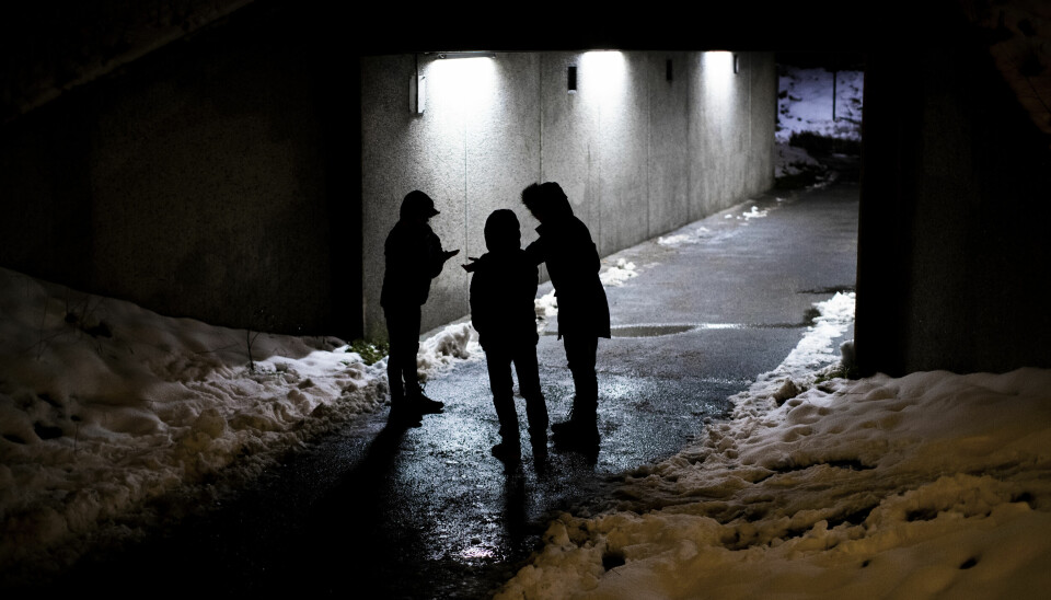 Tre unga personer står i en gångtunnel i mörkret.