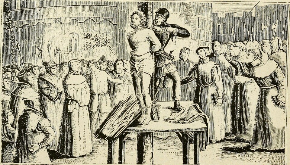 William Tyndale står på en liten plattform, bunden vid en påle.