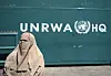 En kvinna i heltäckande sjal står framfår en Unrwa-symbol.