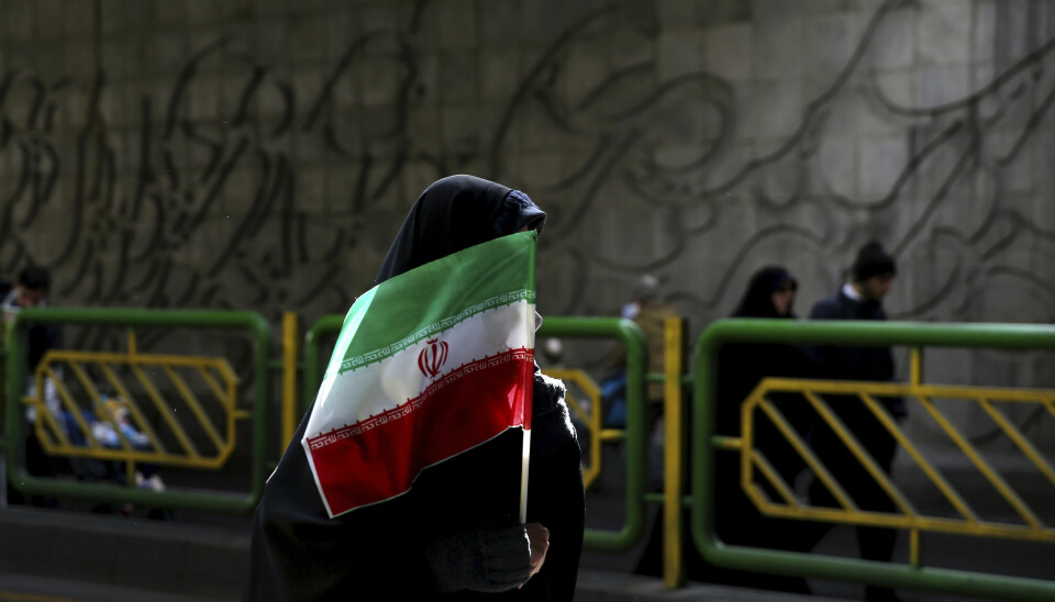 En kvinna med slöja döljer sig bakom en iransk flagga.