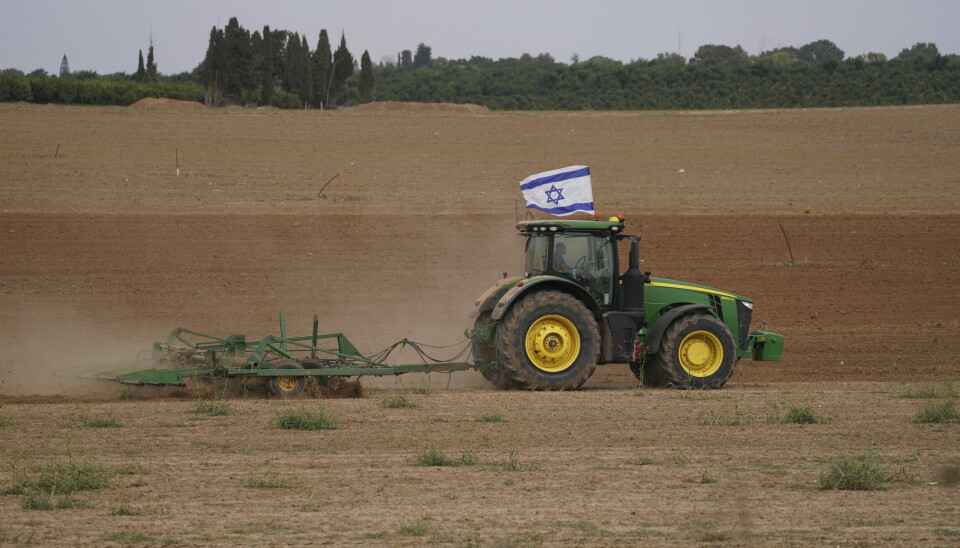 En traktor med en israelisk flagga på taket plöjer en åker.