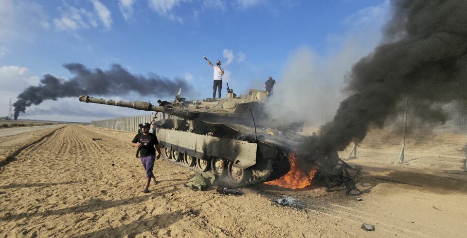 Palestinians celebrate by a destroyed Israeli tank at the Gaza Strip fence east of Khan Younis southern Saturday, Oct. 7, 2023. The militant Hamas rulers of the Gaza Strip carried out an unprecedented, multi-front attack on Israel at daybreak Saturday, firing thousands of rockets as dozens of Hamas fighters infiltrated the heavily fortified border in several locations by air, land, and sea and catching the country off-guard on a major holiday. (AP Photo) DV141