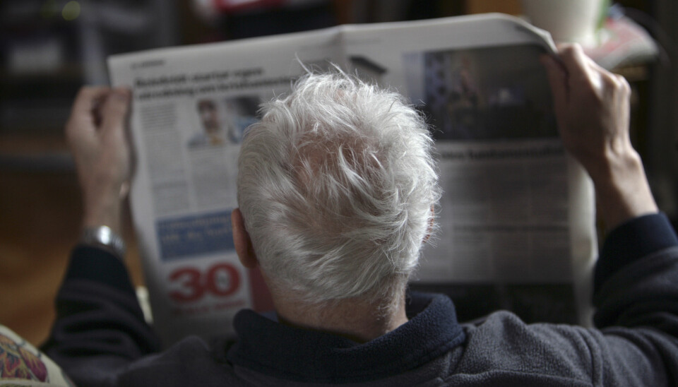 En gråhårig man i morgonrock läser sin morgontidning.