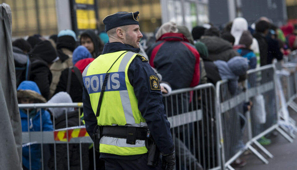 En polis övervakar kön av ankommande flyktingar i snålblåsten vid Hyllie station i Malmö hösten 2015.