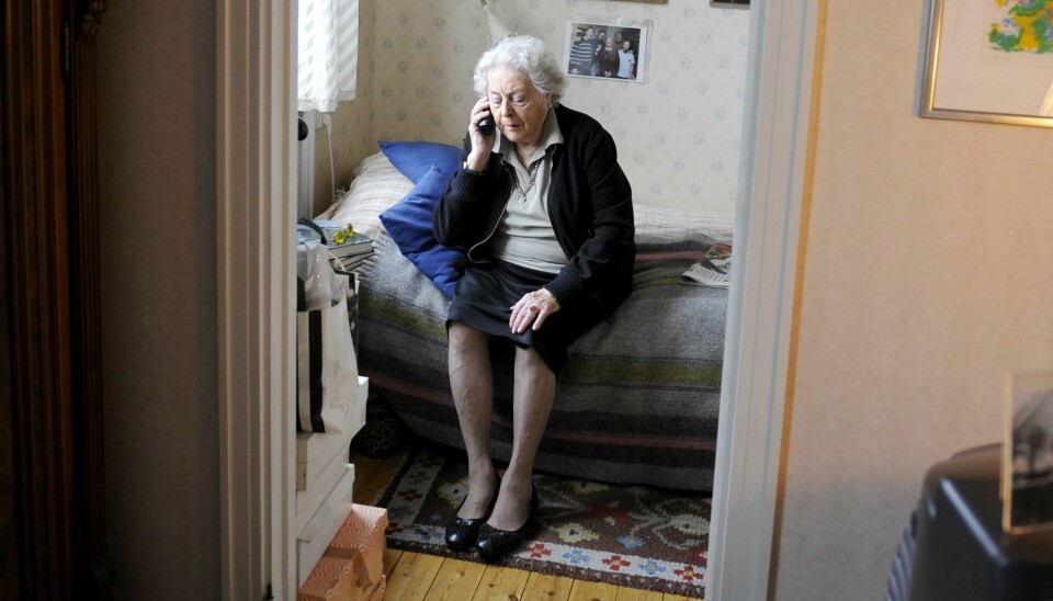 En äldre kvinna sitter på sin säng och talar i sin mobiltelefon