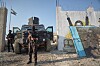Två maskerade kurdiska säkerhetssoldater med vapen vaktar framför ett militärfordon vid en mur i Kobane.