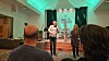 En man och en kvinna talar på en scen framför ett stort grönbelyst kors i en kyrka inför en publik.