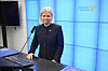 Magdalena Andersson står vid en talarstol i riksdagen framför en blå belyst skärm med logotypen Sveriges riksdag.