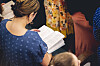 En kvinna i blå prickig tröja läser i en bibel under en samling.