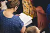 En kvinna i blå prickig tröja läser i en bibel under en samling.