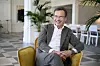 Ulf Kristersson i grå kostym sitter leende i en gul fåtölj i en ljus lokal.