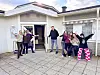 En grupp ungdomar och ledare poserar glatt utanför en ljus träbyggnad med öppna dörrar.