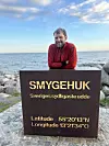Man i orange tröja lutar sig mot monumentet i Smygehuk som markerar Sveriges sydligaste udde.
