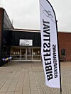 En vit flagga med texten Oskarshamns Bibelfestival framför ingången till en byggnad med samma skylt.