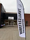 En vit flagga med texten Oskarshamns Bibelfestival framför ingången till en byggnad med samma skylt.