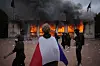 En demonstrant svept i fransk flagga framför en brinnande turistbyrå med kraftig rökutveckling under en protest i Lyon.