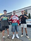 Tre unga män i streetwear och kepsar poserar på en asfalterad parkeringsplats.