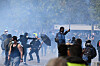 Demonstranter i tårgas under en protest i Paris, en person sparkar i luften och en annan håller ett paraply.