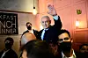 Benjamin Netanyahu vinkar med höjd hand omgiven av säkerhetsvakter med munskydd under ett valmöte.