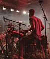 En trummis sedd bakifrån spelar på en rökig scen med röd belysning under en livekonsert.