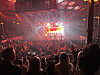 Publik i en fullsatt arena som ser på ett liveframträdande på en starkt belyst scen.