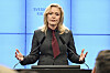 Elisabeth Thand Ringqvist talar vid ett podium med mikrofoner framför en blå bakgrund med texten Sveriges riksdag.